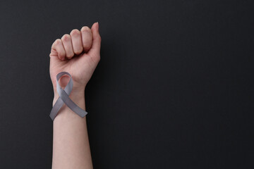 Woman with grey awareness ribbon on black background, top view. Space for text