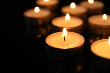 Many burning tealight candles on black background, closeup