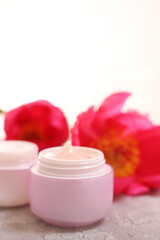 Jars of creams and peony flower on gray table against light background, closeup. Space for text