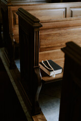 Vertical no people shot of Bible book and rosary beads on wooden pew in Catholic church, copy space