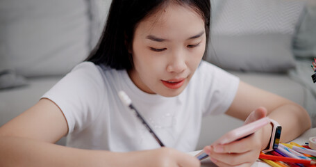 High angle view, Young Asian woman sitting on the floor uses a mobile phone to search for ideas for greeting cards. Holiday hobbies, crafts, DIY cards