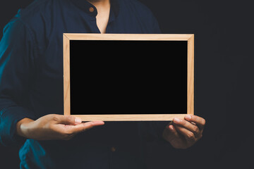 Businessman holding blank chalkboard while standing on a black background.