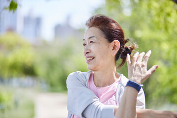 春の新緑の中ストレッチをを行うスポーツウェアをきたシニア女性