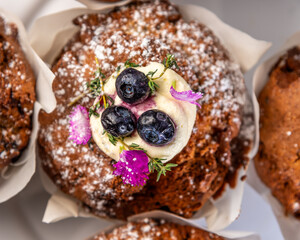 Several muffins on a plate, covered with white icing, blueberries and flowers