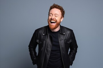 Obraz premium Portrait of a funny red-haired man in a black leather jacket laughing on a gray background.