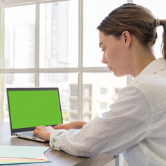 Young woman working at desk using a laptop showing green screen