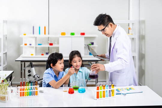 Asian teacher guiding pupils through colorful chemistry experiments in science lab classroom