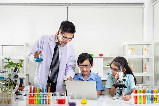 Asian teacher supervising pupils in science experiments with colorful liquids and microscope in the laboratory classroom