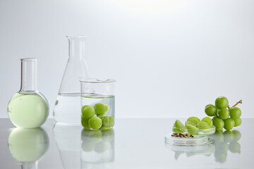 White minimalist background photo with laboratory and green grape featuring. Lab glassware filled by transparent liquid placed on the left, fresh grape and seed on right side, empty space in center