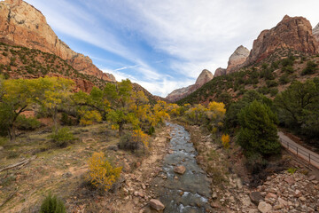 The captivating view of Zion National Parks rugged mountains, flowing river, and colorful fall foliage under clear skies perfectly embodies the beauty of Utahs natural landscapes