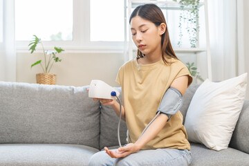 Hypotension problem asian young woman sitting on couch checking high blood pressure and heart rate...