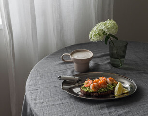 Breakfast served, brunch - sandwich with avocado and shrimp, cappuccino on a round table in the living room