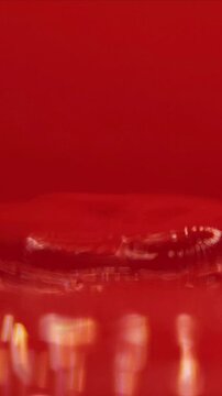 Drop of Water Hitting Water Surface Bouncing Back Making Waves High Speed Macro Close Up. Isolated On Red Background, Vertical Slow Motion Video.