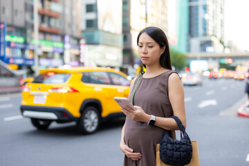 Pregnant woman in the city use cellphone to order taxi and wait in the street of Taipei