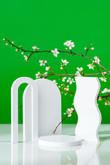 Decorative podiums and blooming branches on green background with shadows