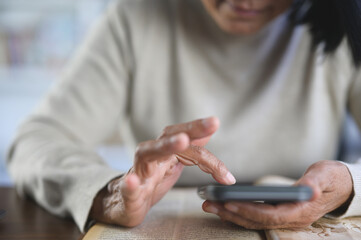 An elderly woman, deeply engrossed, swipes her finger on her smartphone screen, browsing social media.