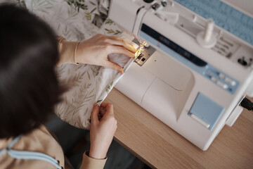 Focused craftswoman sewing with a machine in a cozy workshop.