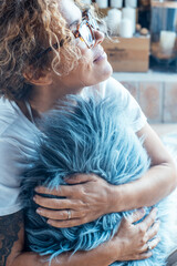 Fototapeta premium One woman embracing pillow at home looking outside the window. Love emotion concept and daydreaming femalepeople in indoor leisure activity alone