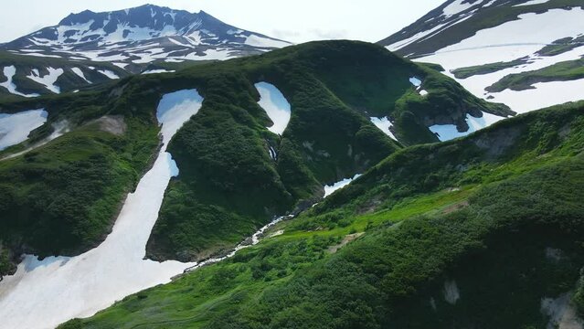 Small valley of geysers in Kamchatka, Russia. Green mountains and volcanoes with snow. Aerial drone view. Beautiful summer landscape. 
