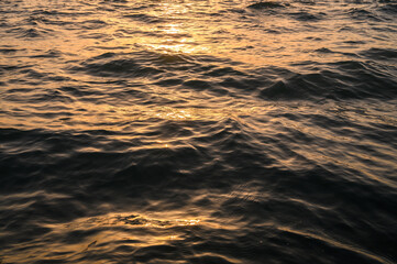Close-up of golden water with calm ripples. Sunset colors
