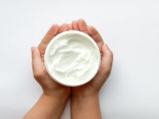 Close up of childs hands holding container of hand cream on white background. Skincare and moisturizing concept. Design for healthcare, beauty, wellness, and child care poster