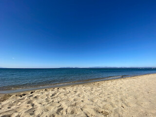 The beach of luxury hotel. Sunny day, calm waveless sea, blue sky. Soft yellow-gold brown-gold sand shines on beach. sea ​​waves hitting the seashore. clear and clean sea water. Balıkesir in Turkiye