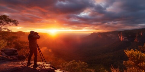 This image captures a photographer standing on a scenic overlook, aiming his camera to capture a breathtaking sunset over a beautiful, expansive natural landscape.