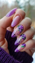 A woman holding purple nails with flowers and glitter.