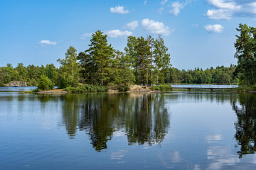 Beautiful Scenery of Scandinavia. Green island with bridge. Stockholm Archipelago. Peaceful view of Lake shore at summer  time. Horizon. View of blue lake surface with perfect reflections. 