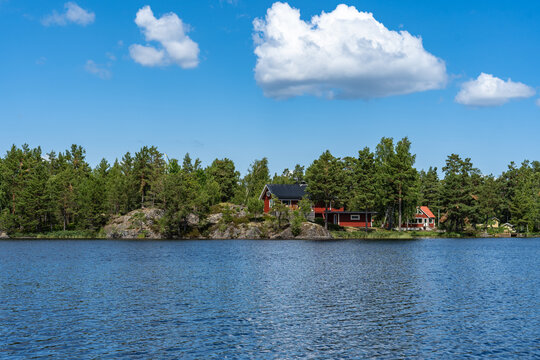 Beautiful panoramic view of the lake or the bay of the Baltic Sea. The rocky shores are covered with forests pines, spruces, firs, coniferous trees. Typical Scandinavian wooden red house on the coast.