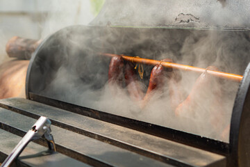 Smoked sausages hanging on rack in a offset smoker with a thick smoke, closed up