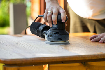 Grinding with an electric wood grinder, restoration of solid wood furniture. Woodwork. Close up of sanding a wood with orbital sander at workshop