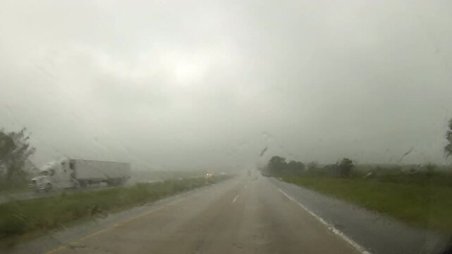Driving point-of-view traveling in rainy conditions on highway with windshield wipers.