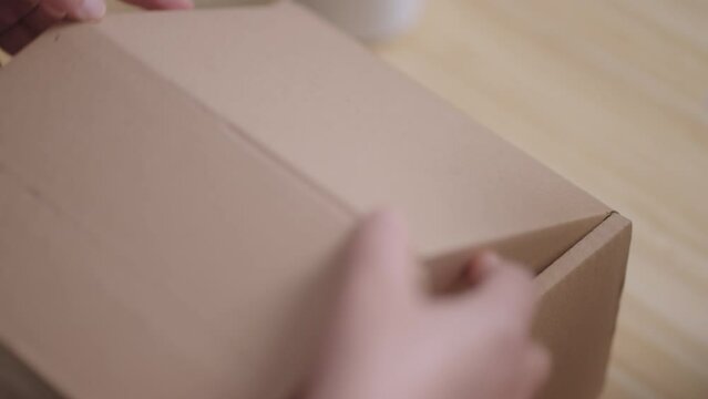A woman places a "100% Recyclable Materials" label on a cardboard box filled with eco-friendly water hyacinth cushioning, demonstrating sustainable and environmentally friendly business practices