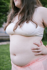 Obese young woman holds her belly. Outdoor exercises