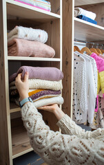 Woman choosing outfit from large wardrobe closet with stylish clothes and home stuff