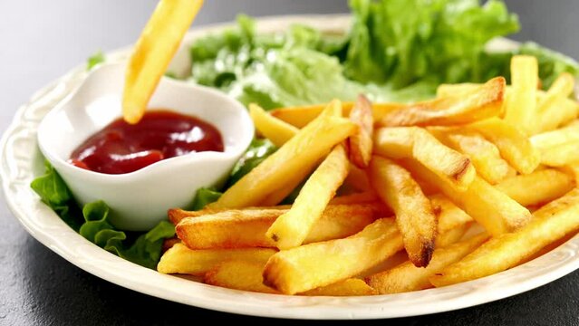 hand dipping french fries in tomato sauce or ketchup