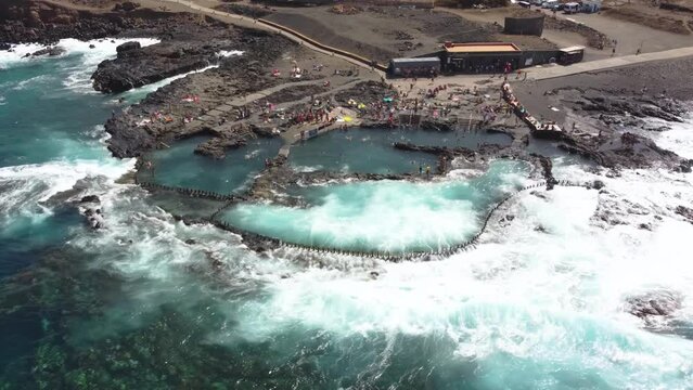 Zoom in from drone point of view of natural pool in the rocky coast of Agaete, a town in the north of the island of Gran Canaria, with people enjoying bathing in the transparent waters