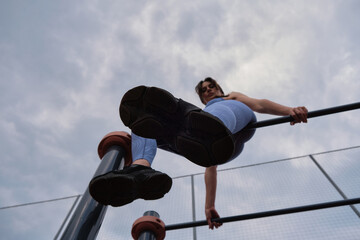 woman, dressed in blue athletic gear, executes a pull-up on a bar, showcasing her upper body strength and dedication to fitness. This photo emphasizes the benefits of outdoor calisthenics for overall