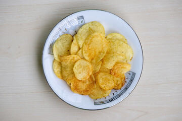 Crispy potato chips on a white plate on wooden background. Crunchy delicious lays potato chips, American style cream and onion flavor. Top view.