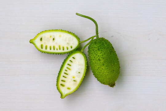 Sliced and whole spiny gourd green vegetable on light white wooden background. Momordica dioica is also known as Kakrol, Kartoli, Kankoda, Kantola. Top view.