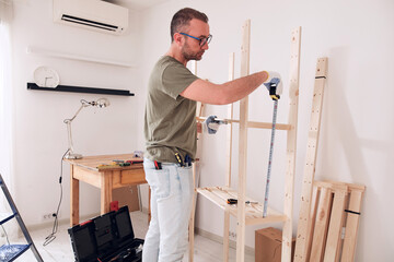 Man assembling new wooden shelf and furniture in the apartment.