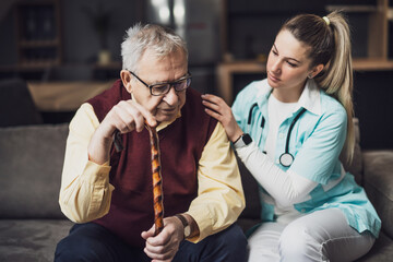 Nurse home caregiver is assisting old man at his home. Professional health support for elderly people.