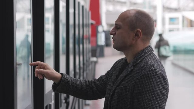 A man is interacting with a touchscreen information display in a modern transport hub