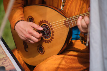 A minstrel plays an oud lute, hands on strings in close-up