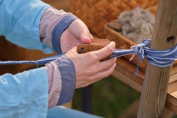 Woman demonstrates the art of tablet weaving, producing handmade textiles with a wooden tool.