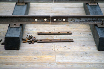 Assembling a railway track, aligning a metal rail with a fishplate. Several bolts and nuts lie on the wooden platform beside them.
