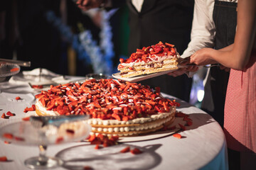 bride and groom cutting big wedding cake. On top its covered with strawberries.