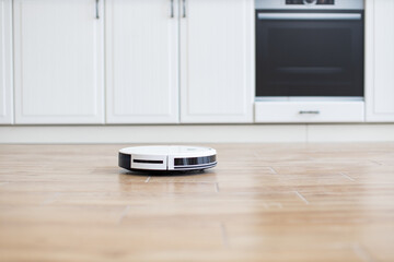 Robotic vacuum cleaning kitchen floor in modern home. Automated cleaning device on wooden floor contributes to smart home technology and convenience. Clean, efficient, and modern appliance.