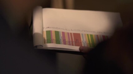 Hand holding a color-coded event planning book list, detailed and organized.